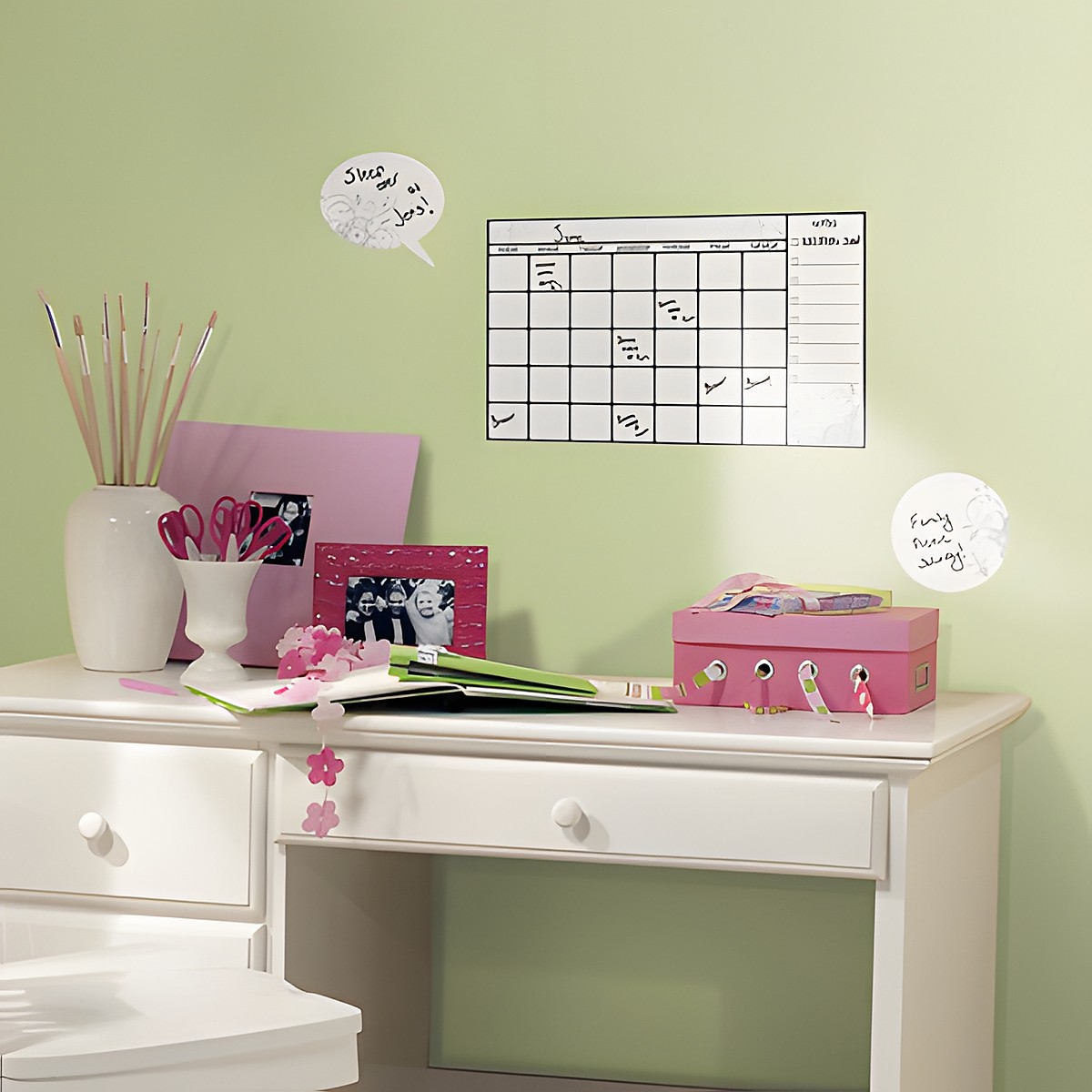RoomMates wiederbeschreibbarer Wandkalender, Monatskalender mit floralem Rankenmuster und Sprechblasen-Notizfeldern an einer grünen Wand über einem Schreibtisch
