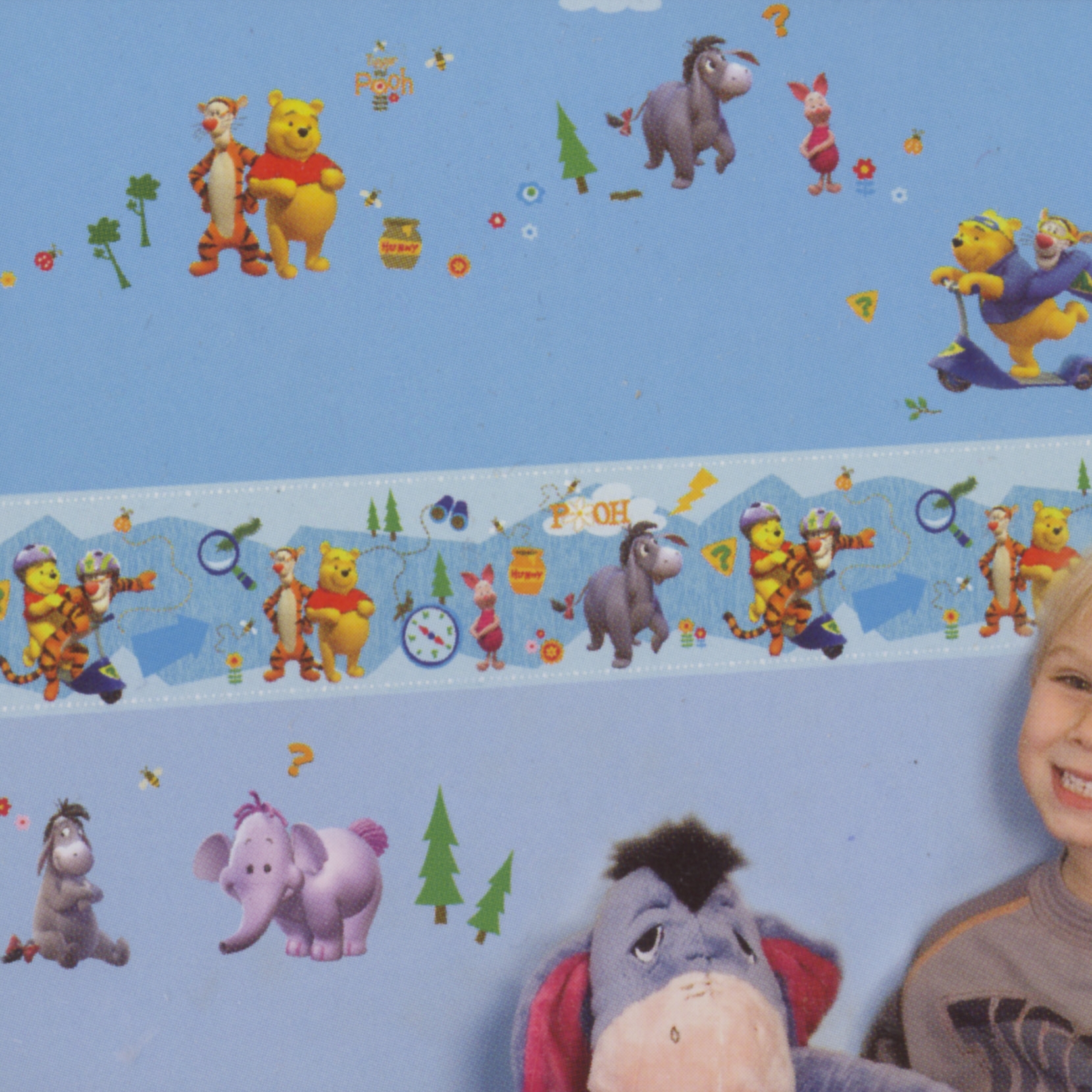 decofun border My Friends Tigger & Pooh on a pale blue children's room wall, with a boy and an Eeyore plush toy in front