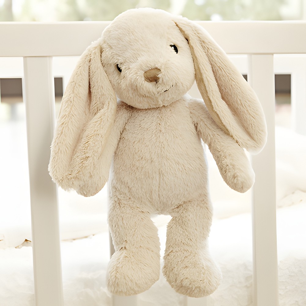 Cloud b Einschlafhilfe Bubbly Bunny, Anwendungsfoto: beiges Hasen-Kuscheltier hängt am Gitterbett