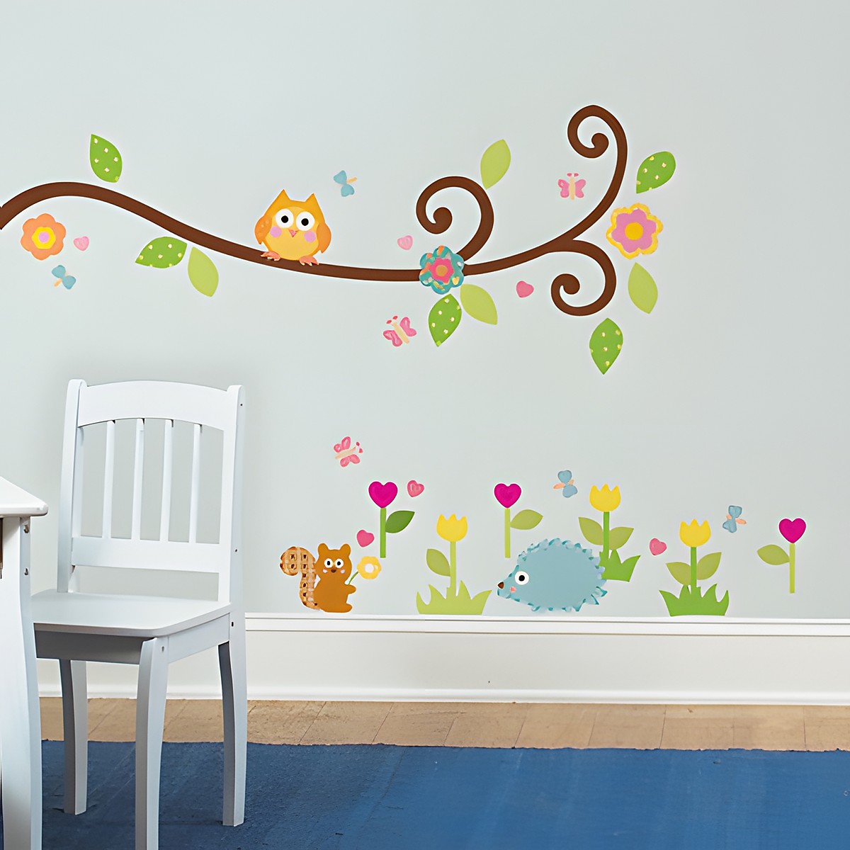 RoomMates Wandbild Happi Scroll Branch, geschwungener Ast mit Eule über Igel- und Eichhörnchen-Motiven an einer grauen Kinderzimmerwand neben einem weißen Stuhl