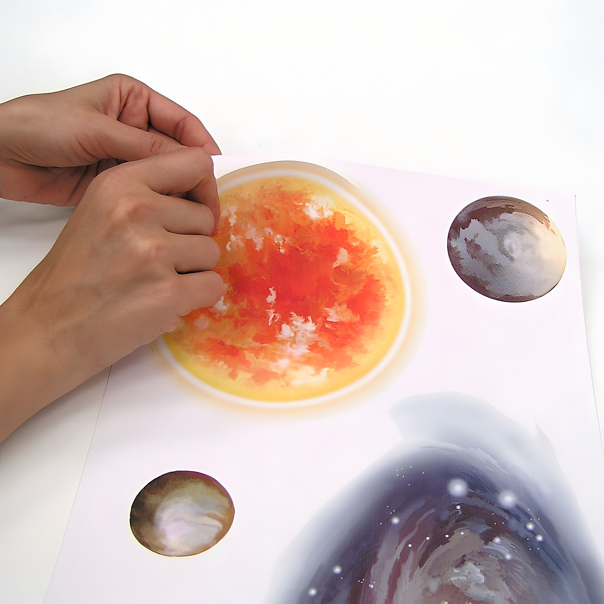 RoomMates wall decal Space Travel, hands peeling a sun motif off the backing sheet next to planet motifs, usage example