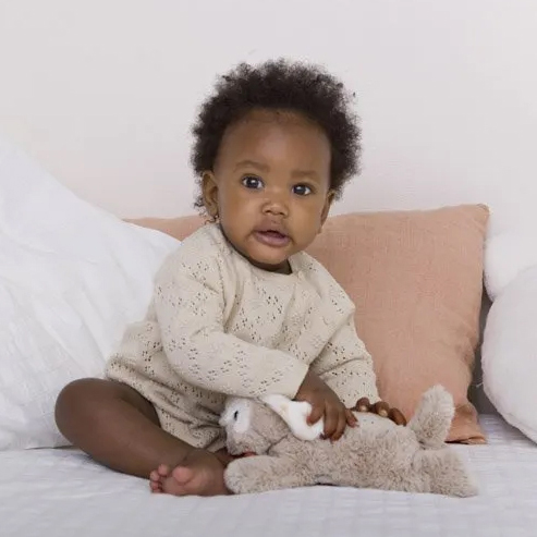 Cloud b sleep aid Dream Buddies dog, lifestyle photo of baby sitting in bed with beige plush toy