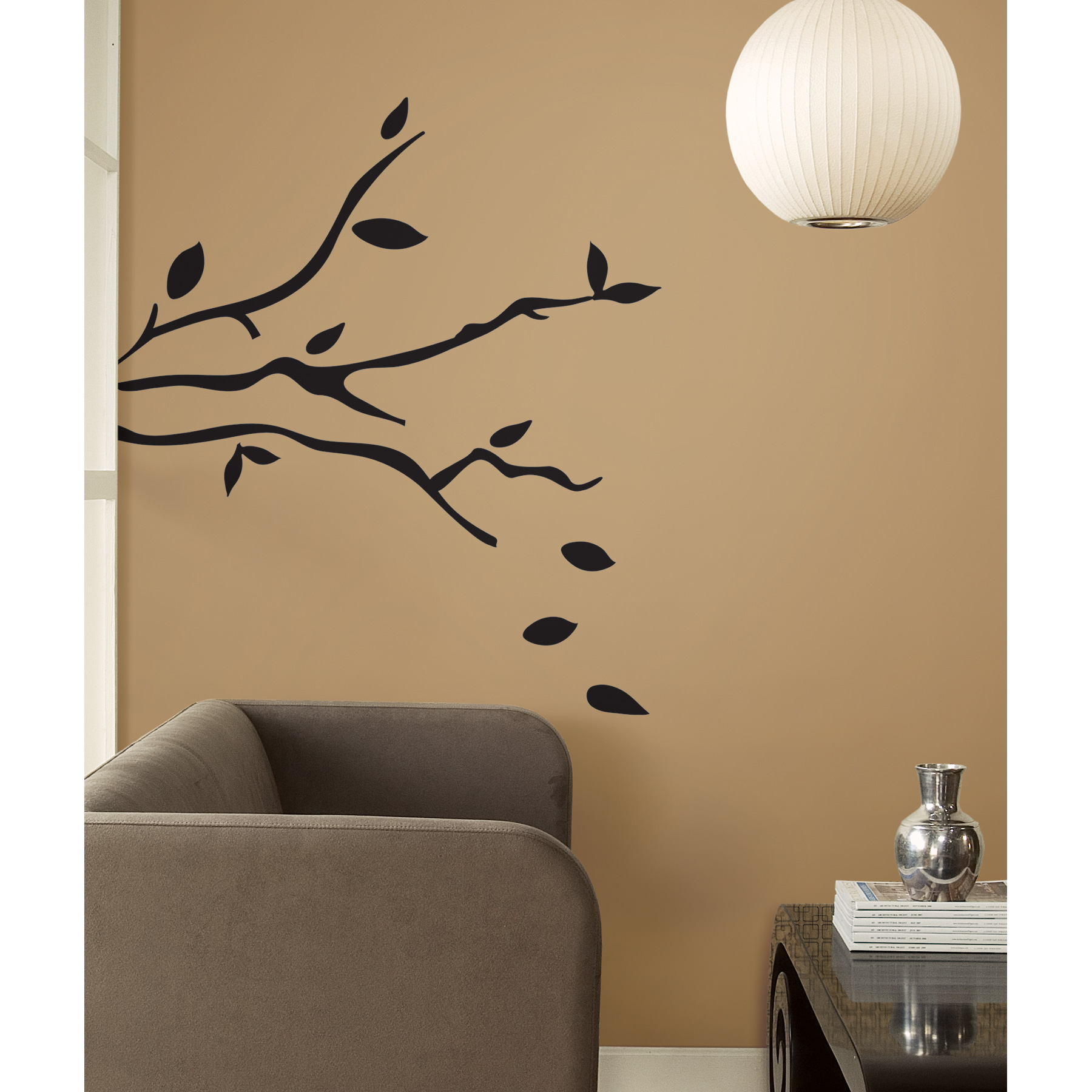 RoomMates wall decal Tree Branches, black branch with falling leaves on a brown wall next to an armchair