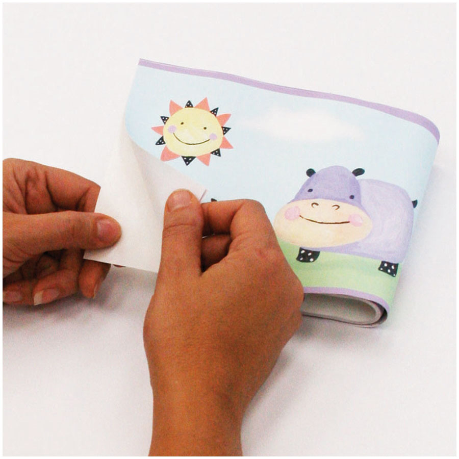RoomMates border Polka Dot Piggy, hands peeling the border strip with a sun and hippo motif off the backing paper, usage example