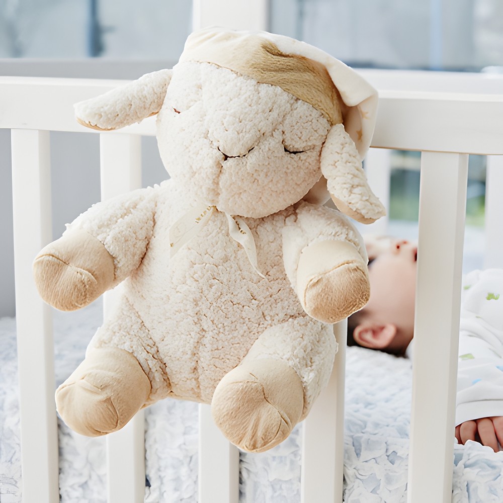 Cloud b Einschlafhilfe Schaf Sleep Sheep, Kuscheltier am Gitterbett mit schlafendem Baby im Hintergrund