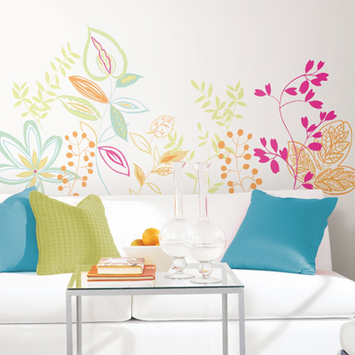 RoomMates wall decal Graphic Leaves, colourful graphic leaf and blossom vines in green, pink and orange on a white wall above a sofa