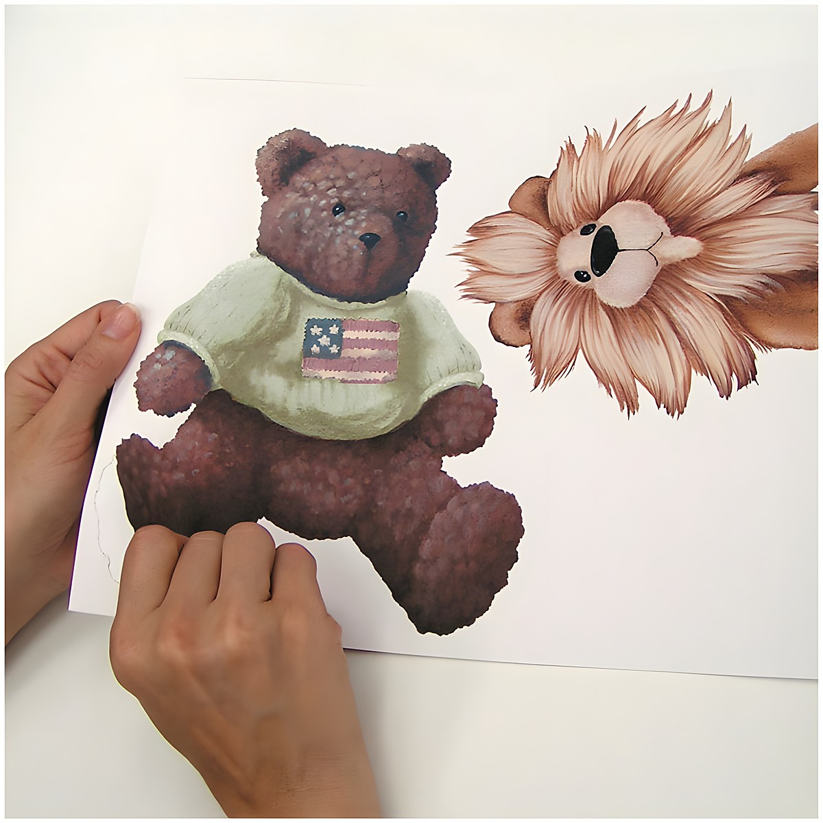 RoomMates wall decal Cuddle Buddies, hands peeling a bear motif wearing a sweater off the backing sheet, usage example