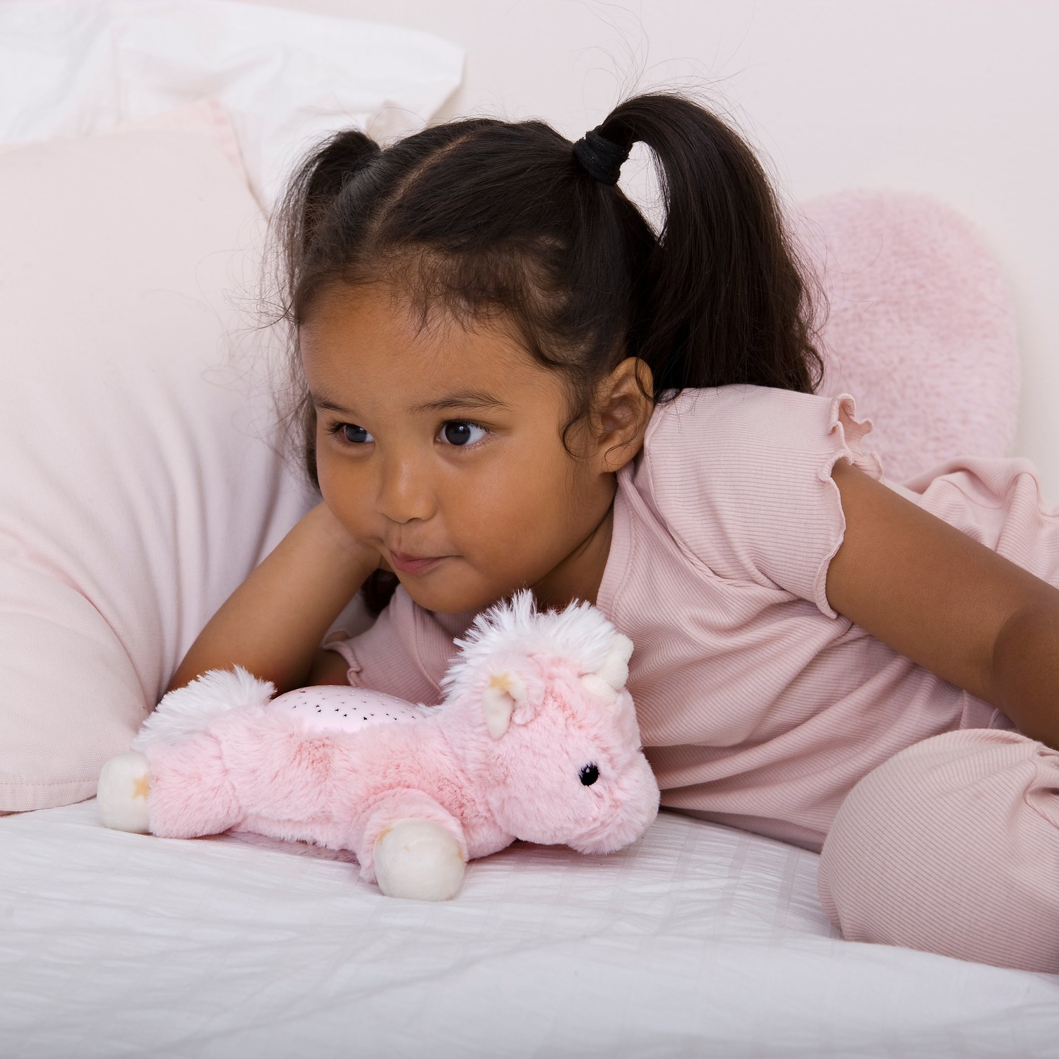 Cloud b sleep aid Dream Buddies unicorn, lifestyle photo of girl with pigtails playing with pink plush toy on bed