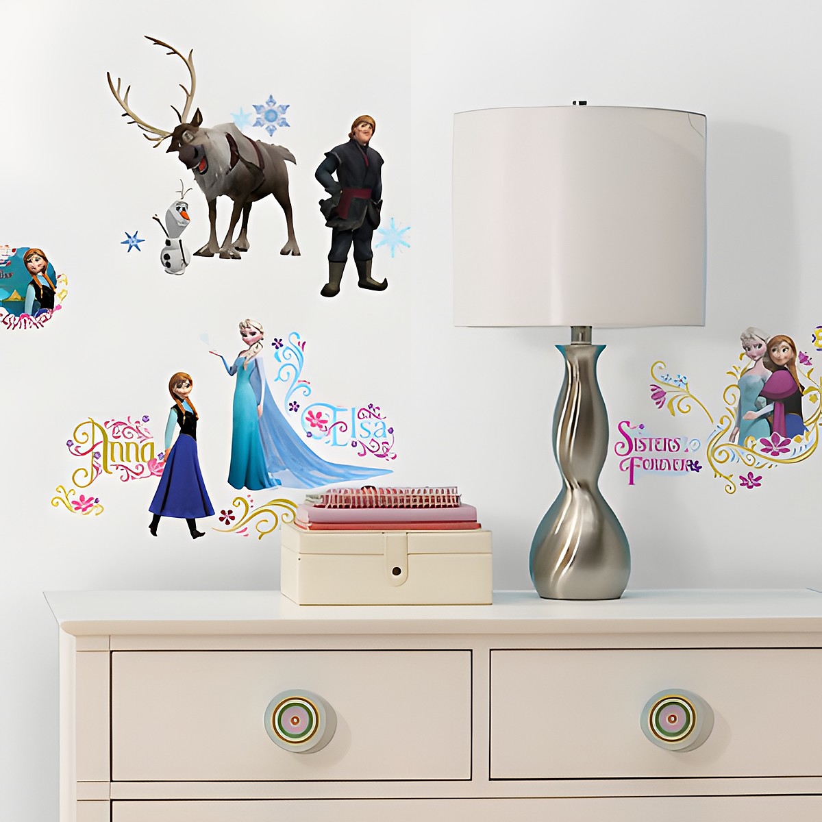 RoomMates Wandsticker Disney Die Eiskönigin, Motive mit Elsa, Anna, Olaf, Sven und Kristoff sowie Schriftzügen an einer weißen Kinderzimmerwand über einer Kommode