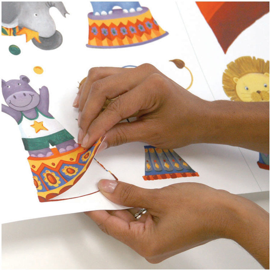 RoomMates wall decal Circus, hands peeling a circus tent motif off the backing sheet, usage example