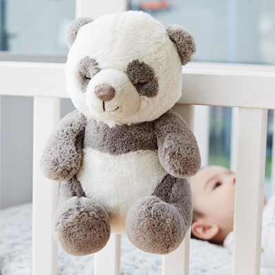 Cloud b Einschlafhilfe Peaceful Panda, Anwendungsfoto: Panda-Kuscheltier hängt am Gitterbett, Baby im Hintergrund