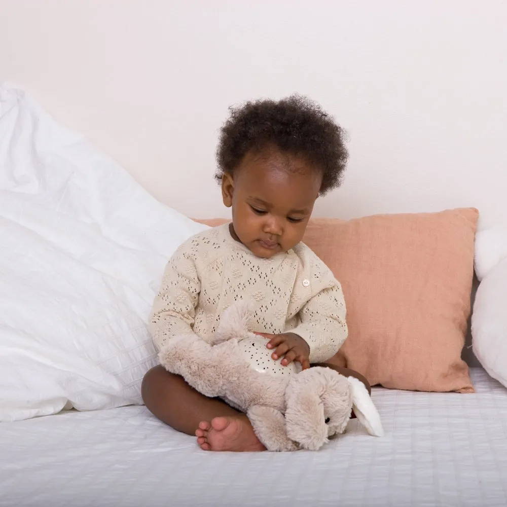 Cloud b sleep aid Dream Buddies dog, lifestyle photo of toddler sitting on bed with beige plush toy