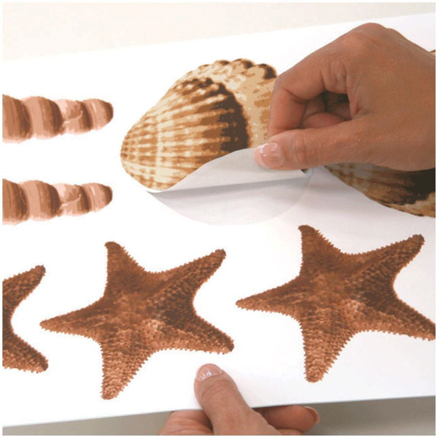 RoomMates wall decal Sea Shells Peel & Stick, hands peeling a shell motif off the backing sheet among starfish, usage example