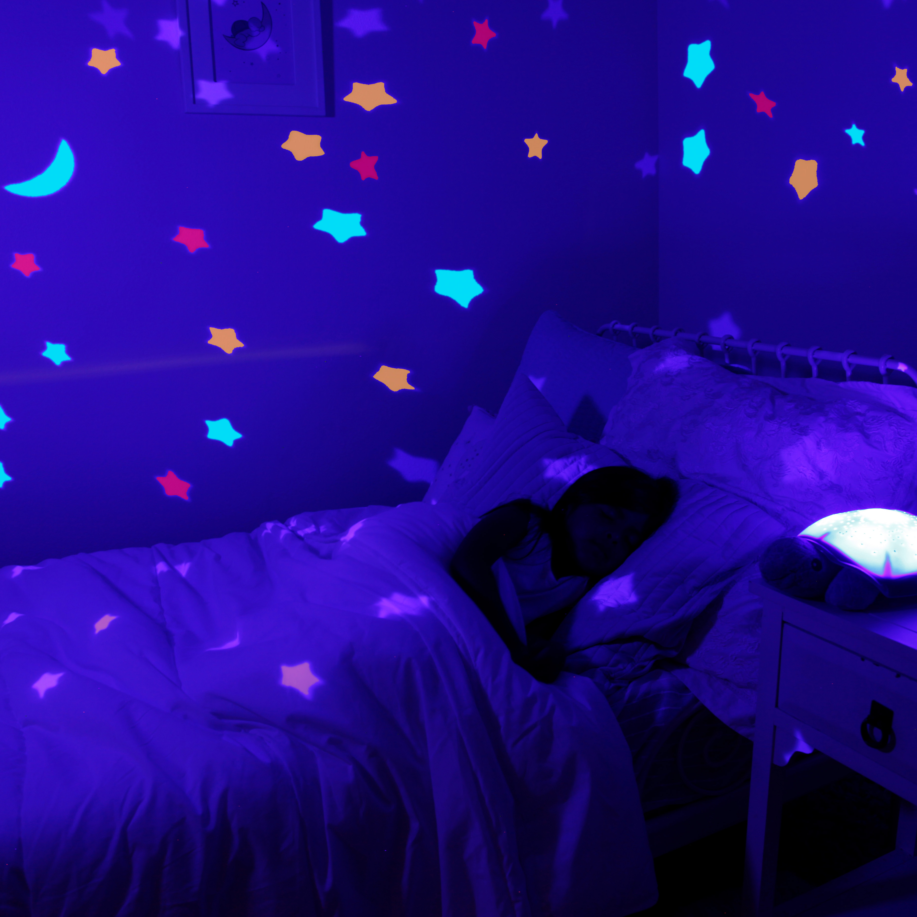 Cloud b sleep aid Twinkling Twilight Turtle Pink, lifestyle photo with colourful star projection in a darkened bedroom