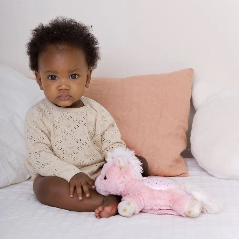 Baby sitzt auf dem Bett neben dem Nachtlicht Dream Buddies Einhorn von Cloud b